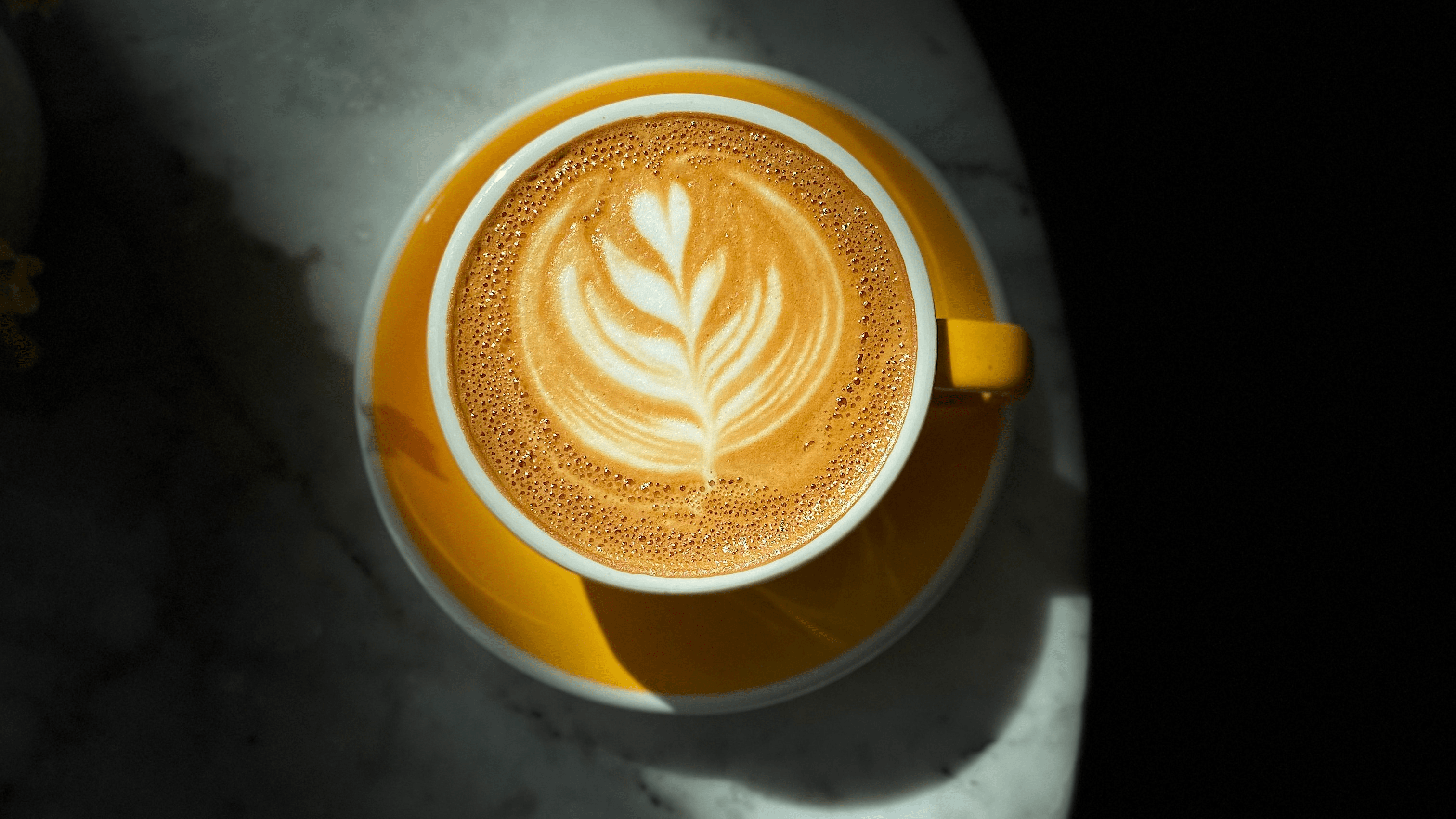 A high contrast photo of a cappuccino in a yellow mug with coffee art.
