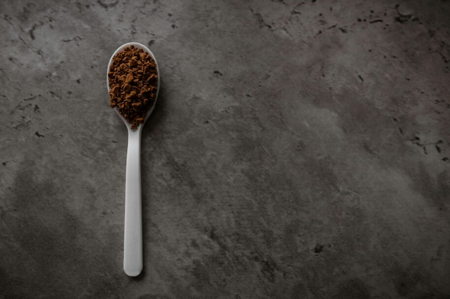 Metal spoon with ground coffee on a concrete background.