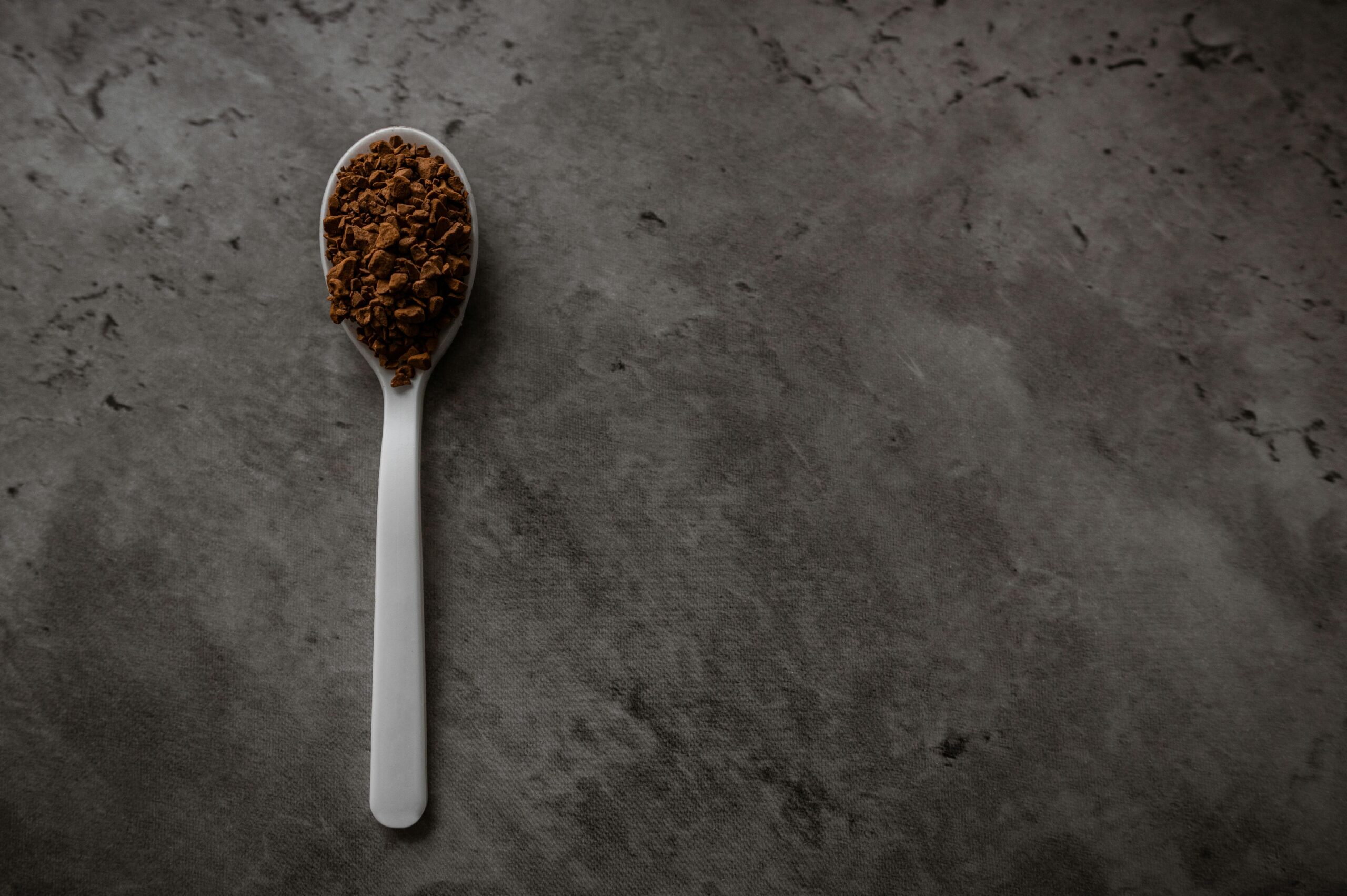 Metal spoon with ground coffee on a concrete background.